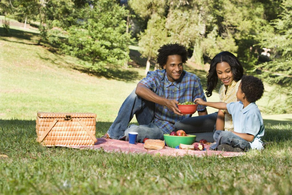 Smiling happy parents and son having picnic in park.