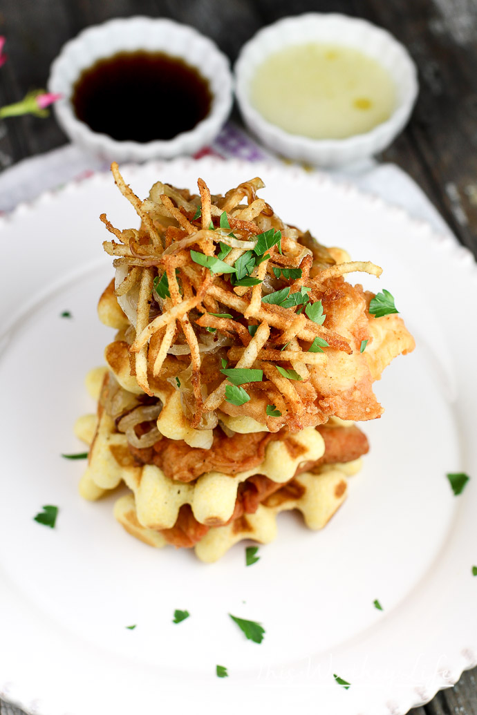 Cornmeal + Buttermilk Waffles With Savory Fried Chicken stacked with potato frites and caramelized onions on white plate