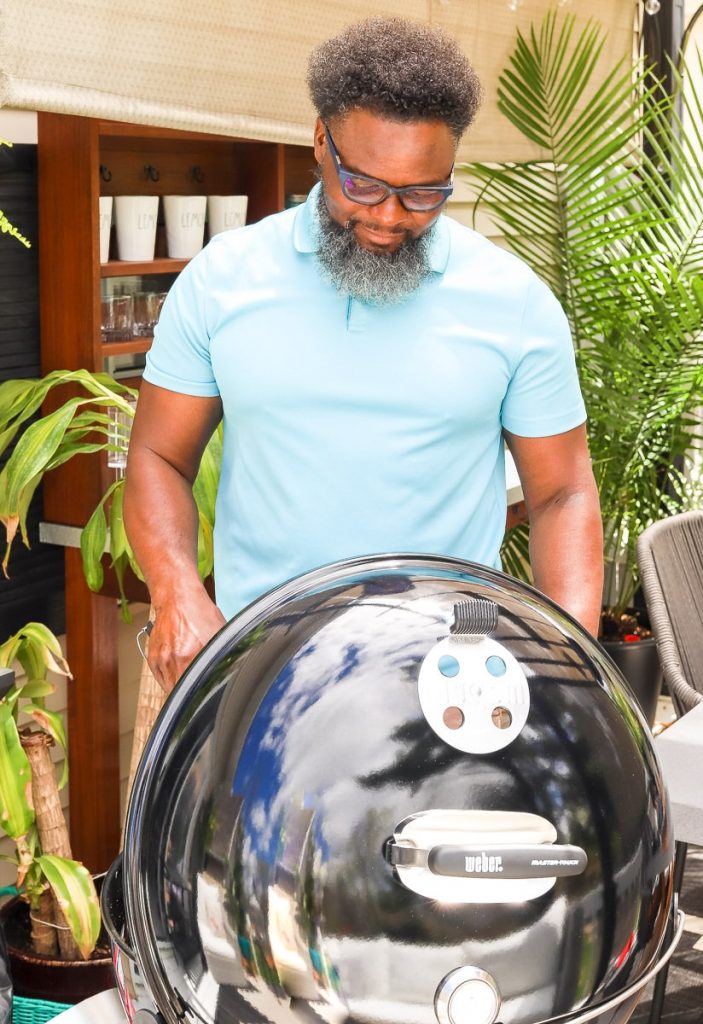 Guy standing over charcoal Weber grill