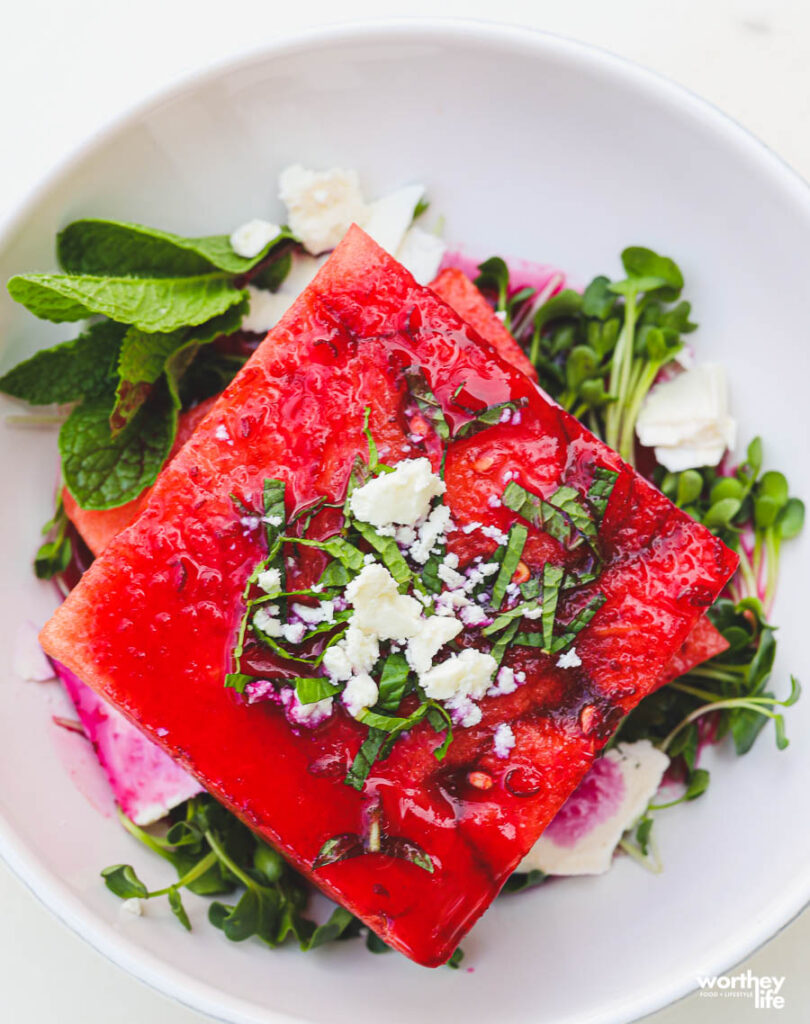 watermelon stacked with feta cheese with green veggies on white plate