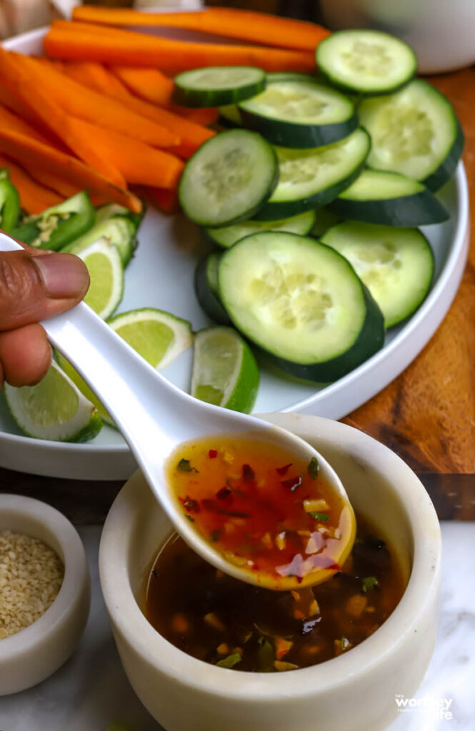 A white plate with vegetables and a small serving bowl of sweet spicy glaze