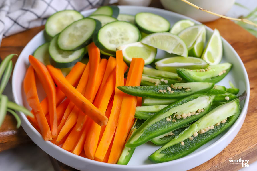 a white plate of sliced carrots, cucumbers, limes, and peppers