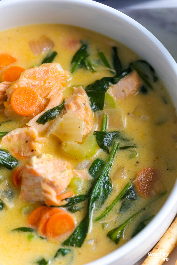 a close up of a white bowl filled salmon and spinach soup