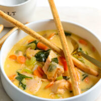 a white porcelain bowl with warm salmon soup and two crossed breadsticks