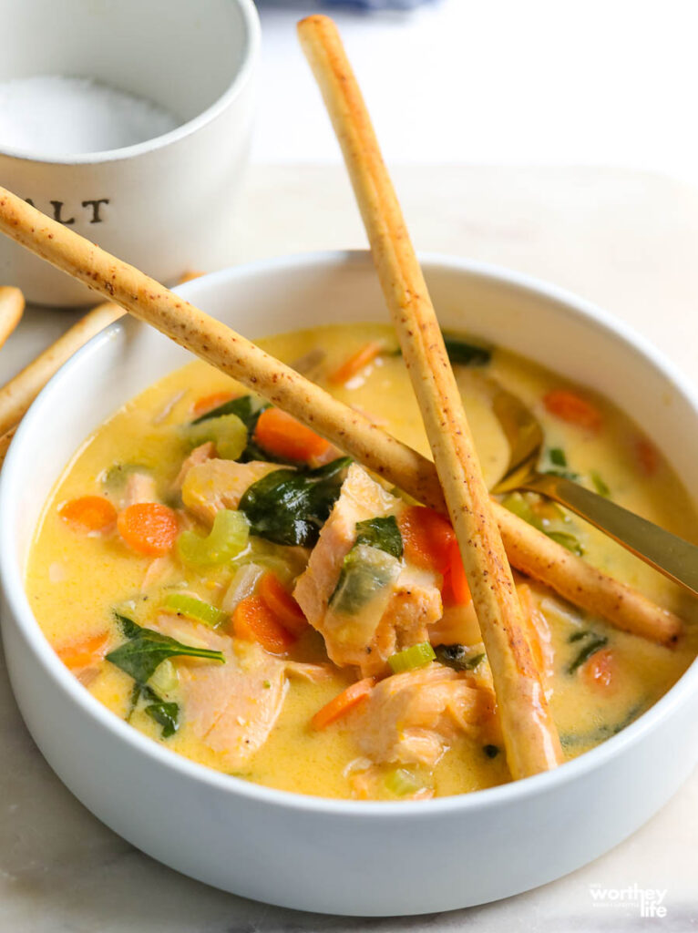 a white porcelain bowl with warm salmon soup and two crossed breadsticks