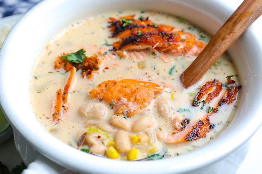 white soup tureen with white bean chili and salmon. topped with green onion and cilantro