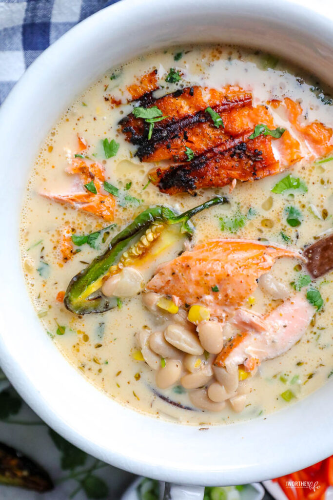 white soup tureen with white bean chili and salmon. topped with green onion and jalapeno peppers