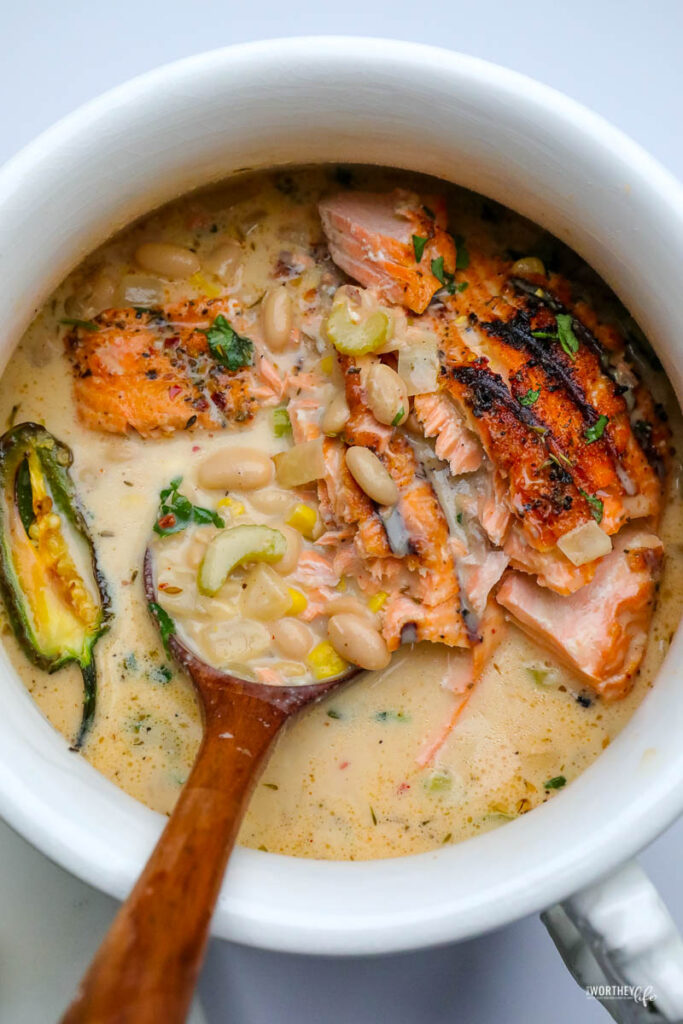 a white soup tureen filled with smoky white salmon chili served with a wooden spoon