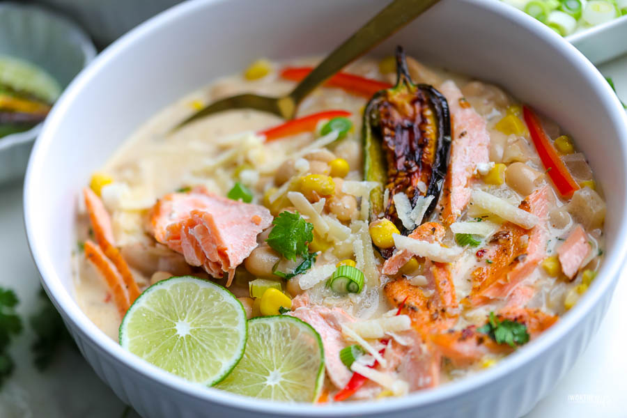 white bowl with white bean chili and salmon. topped with green onion and two wedges of lime