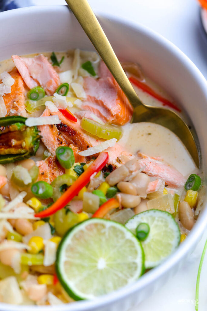 white bowl with white bean chili and salmon. topped with green onion and shredded Mexican cheese