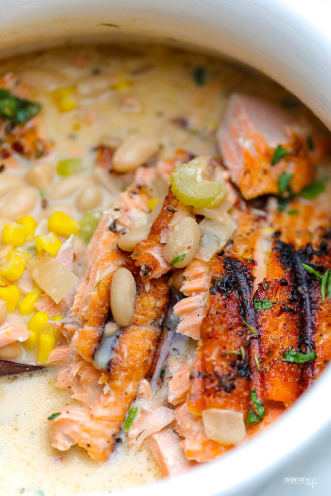 white soup tureen with white bean chili and salmon. topped with green onion and whole kernel sweet corn