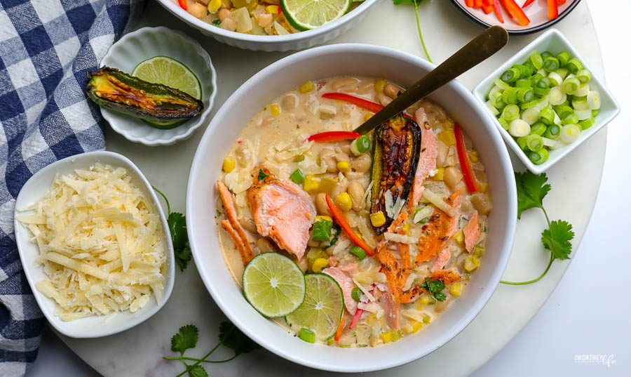 white bowl with white bean chili and salmon. topped with green onion and sliced red peppers