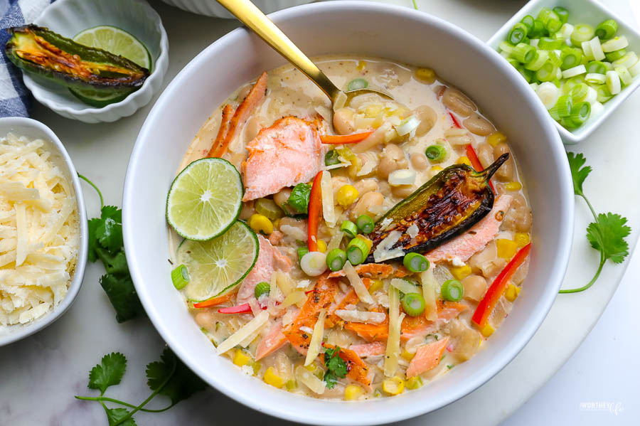 white bowl with white bean chili and salmon. topped with green onion and wedges of lime