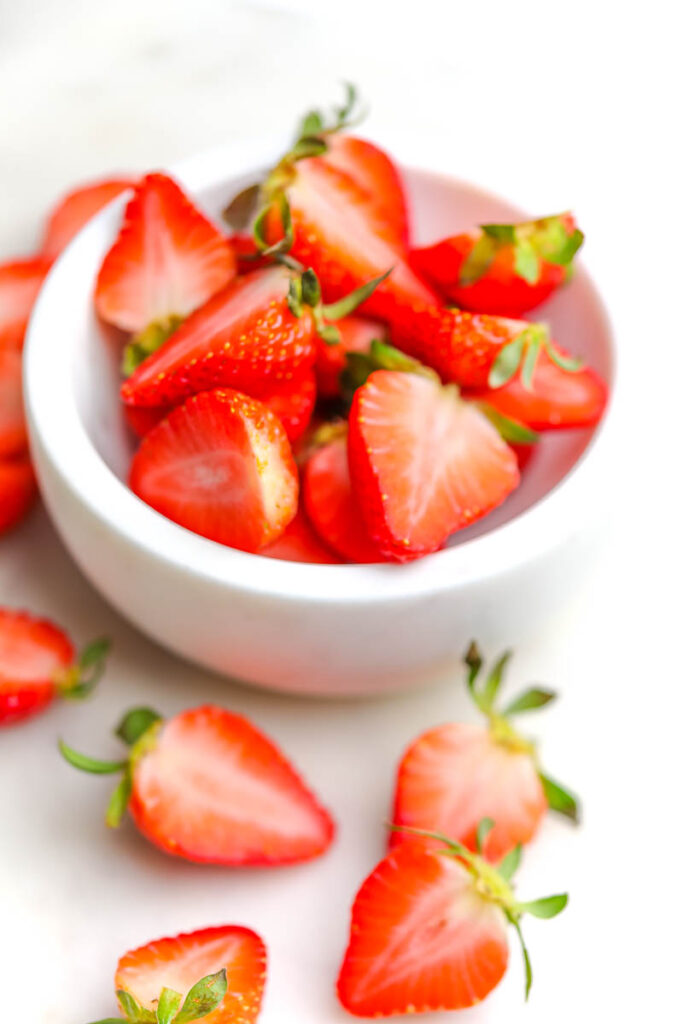 fresh strawberries cut up in a white marble bowl