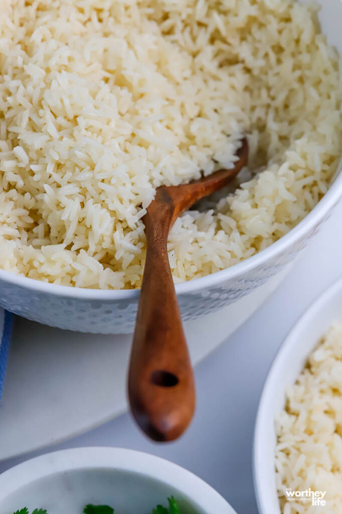 a white bowl filled with rice and a wooden serving spoon