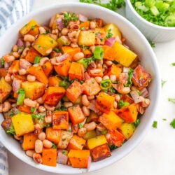 a white bowl filled with sweet potato and black eyed peas hash topped with parsley