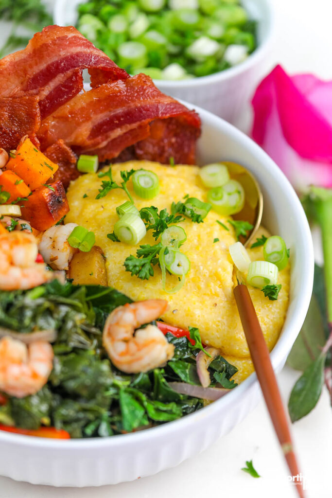 a white bowl with greens, cheesy grits, and bacon