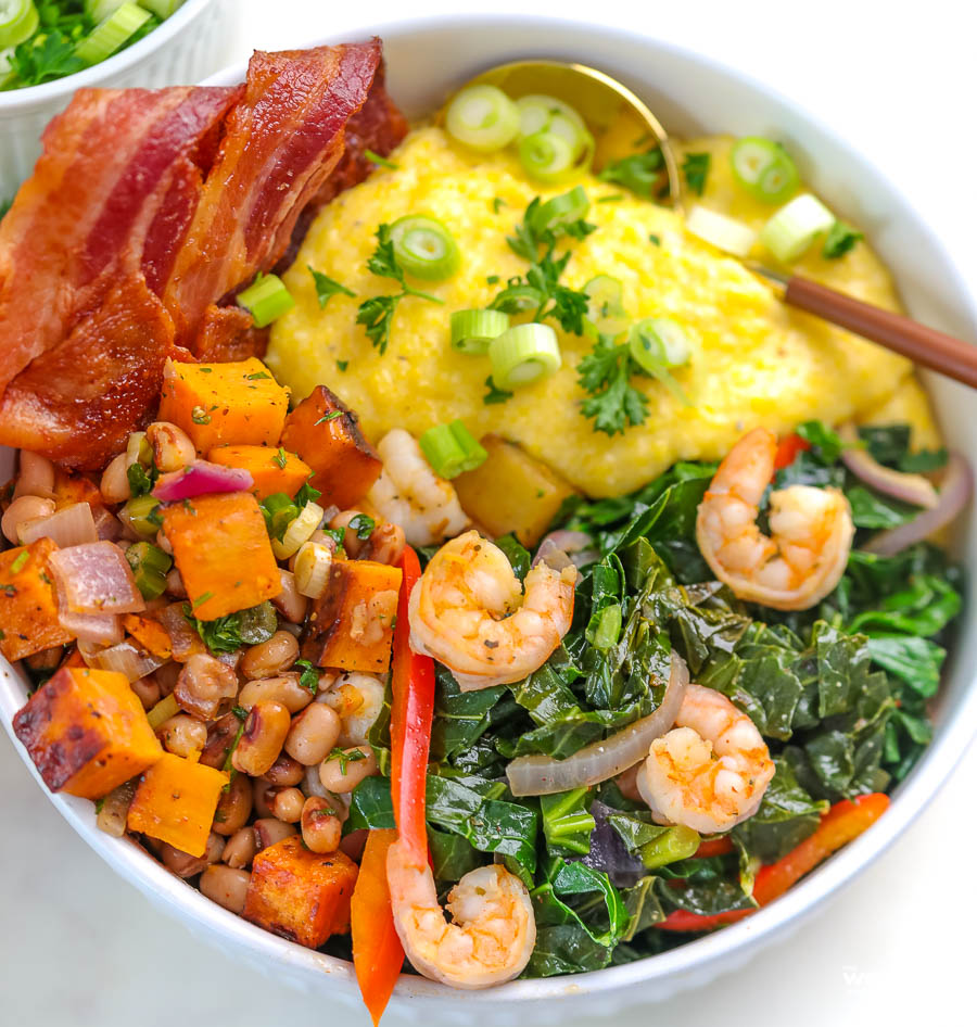 white bowl filled with collard greens bacon cheesy grits shrimp and sweet potato hash