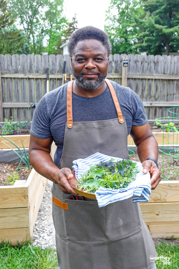 a man wearing an apron holding up a platter of fresh herbs
