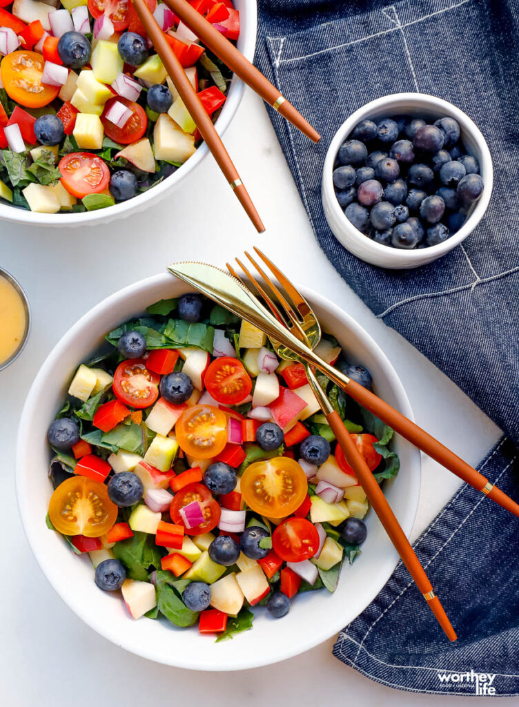 chopped kale and blueberry salad in a white bowl with a fork and knife