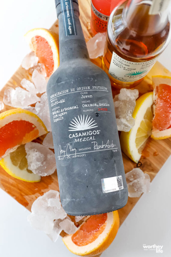 a bottle of mezcal surrounded by sliced paloma fruits