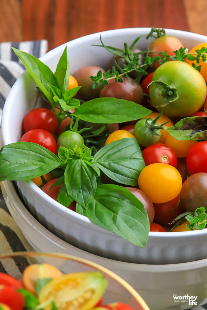 a partial view of a white bowl filed with herbs and tomatoes