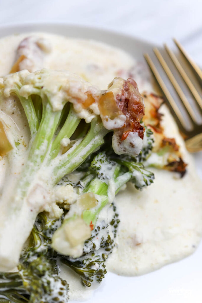 Broccoli with Prosciutto & Cream Gruyère Sauce on a white plate with a fork