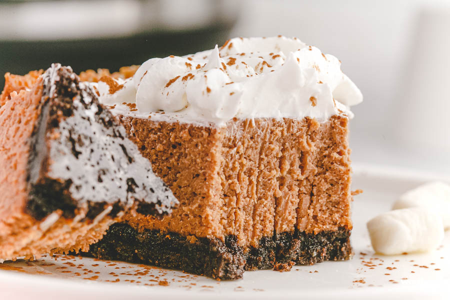 bite of cheesecake on white plate with whipped topping