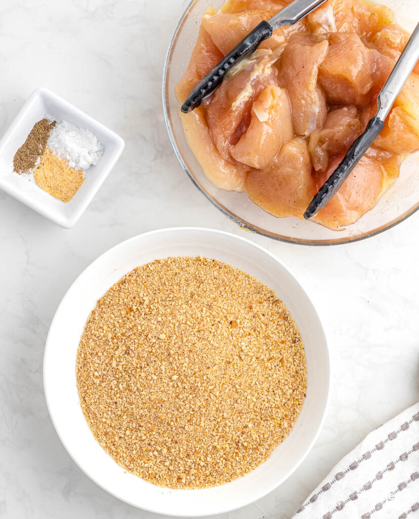 cut up chicken breasts in a bowl with breadcrumbs