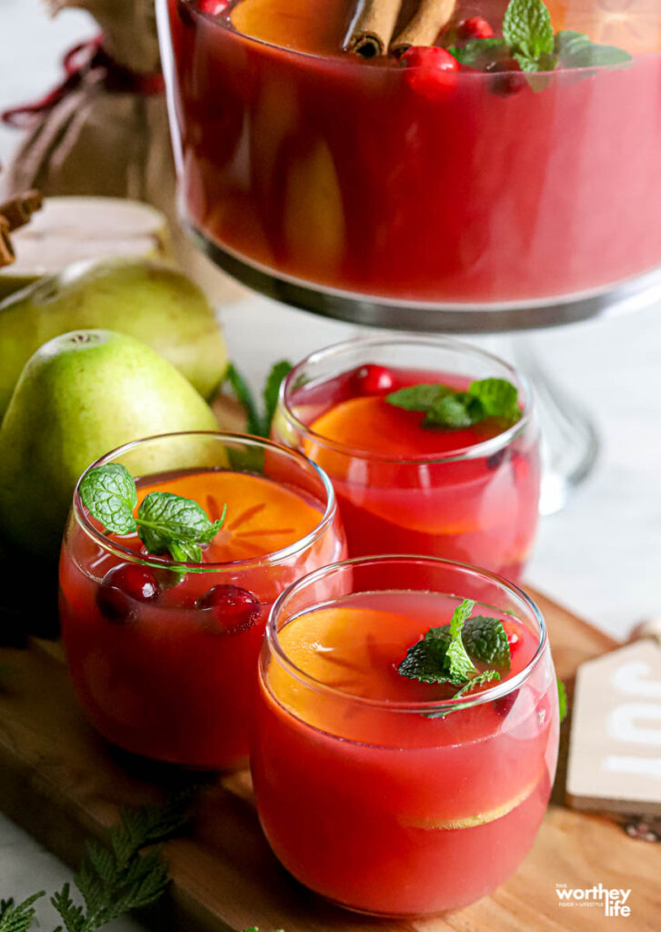 Cups of cranberry ginger ale holiday punch next to a punch bowl