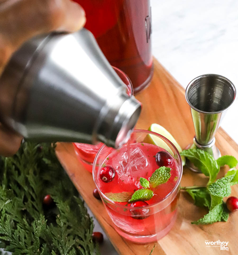 man's hand pouring cranberry mule into a glass