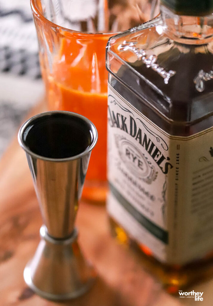 a bottle of rye whiskey, a jigger, and a cocktail mixing glass with a bar spoon