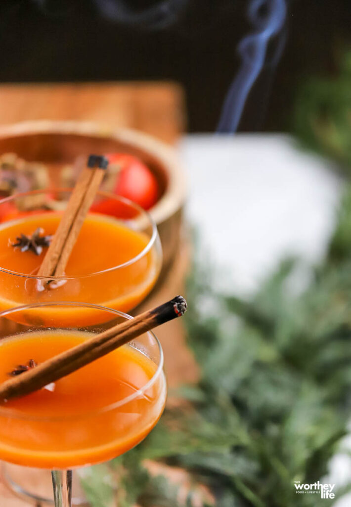 two coupe glasses filled with a persimmon rye cocktail with smoky cinnamon sticks