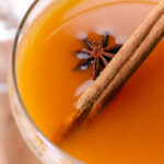 persimmon cocktail in a coupe glass garnished with star anise and a cinnamon stick