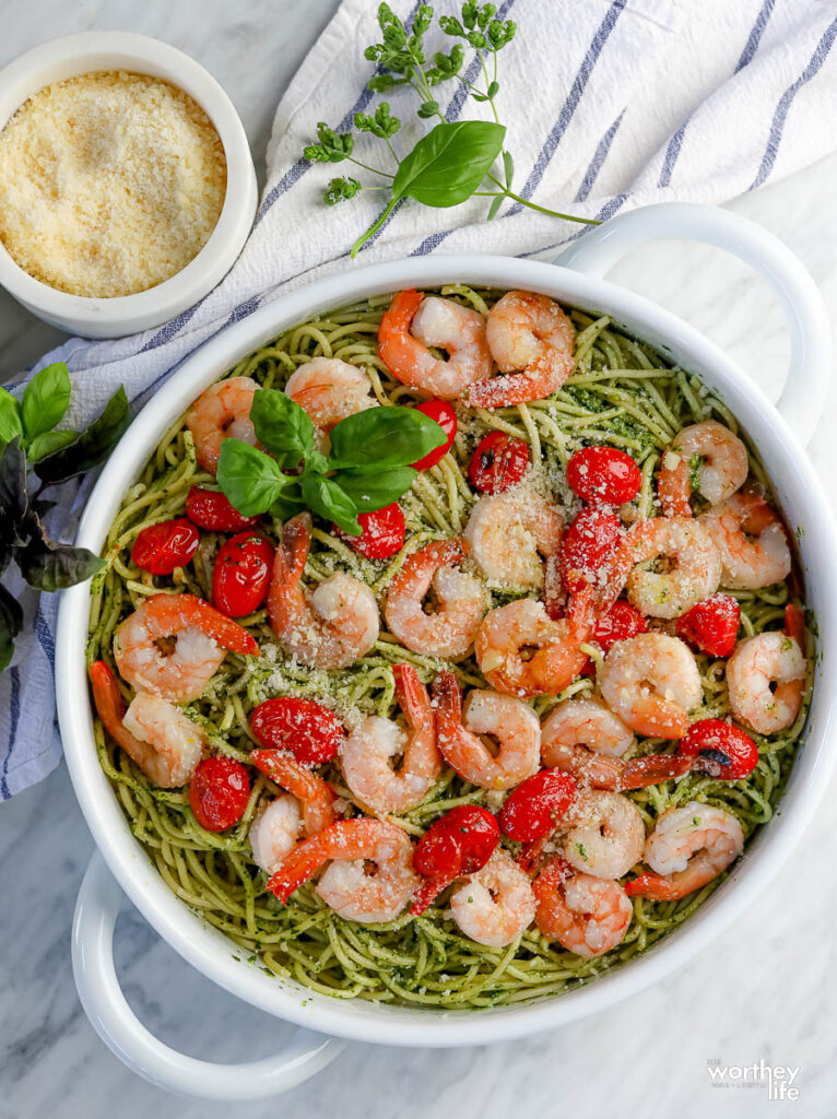 A white serving dish filled with a pesto pasta recipe with shrimp and tomatoes