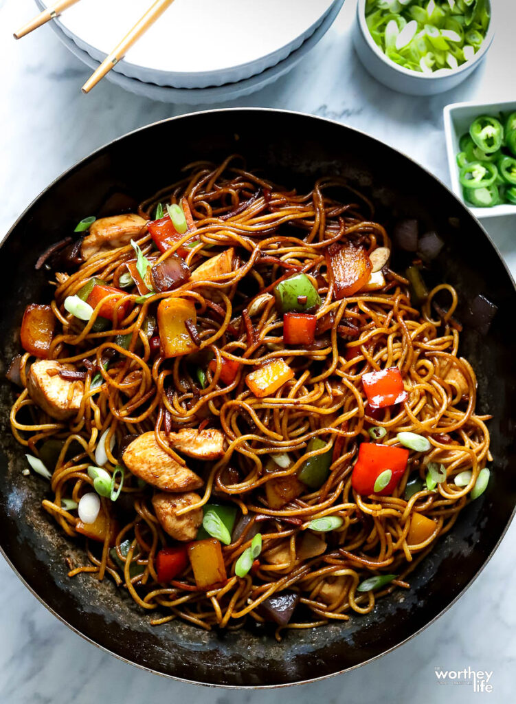Lo Mein prepared in a wok with green onion and peppers on the side