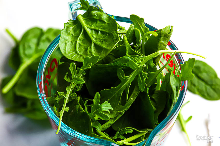 a measuring cup filled with fresh herbs