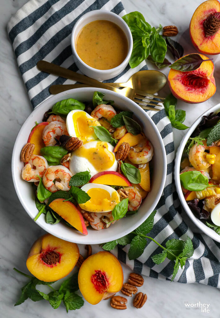 two salad bowl filled with salad, cut peach and peach vinaigrette, blue and white napkin