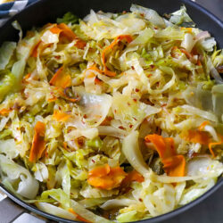 a skillet with fried cabbage, onions, and carrots