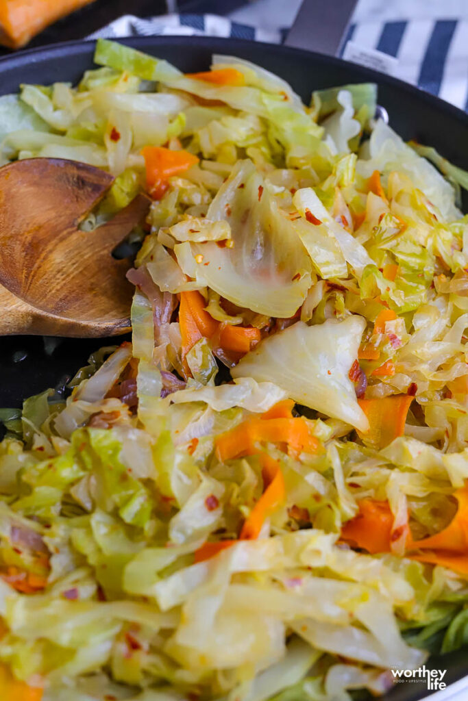 Fried cabbage in a skillet with a wood serving spoon