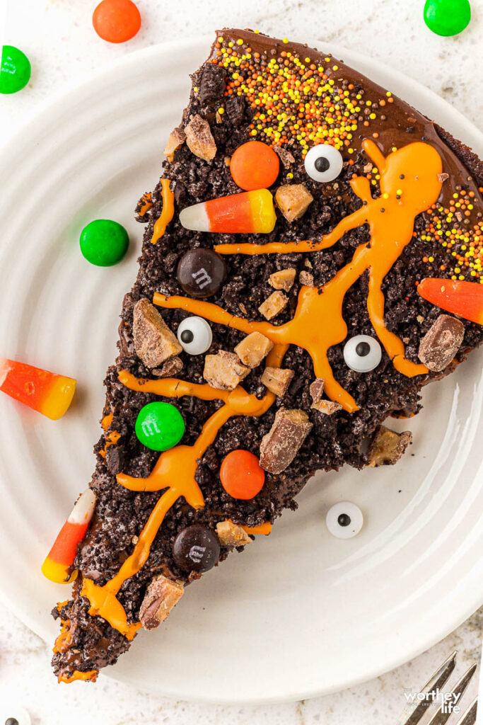 slice of brownie with candy and orange frosting on white plate