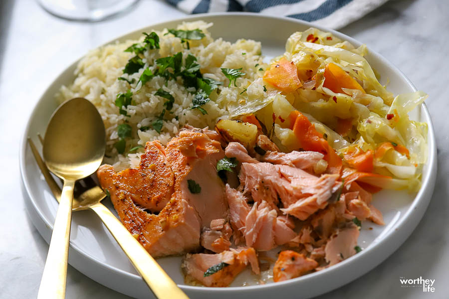 a plate with salmon, fried cabbage, and herb rice with a spoon and fork
