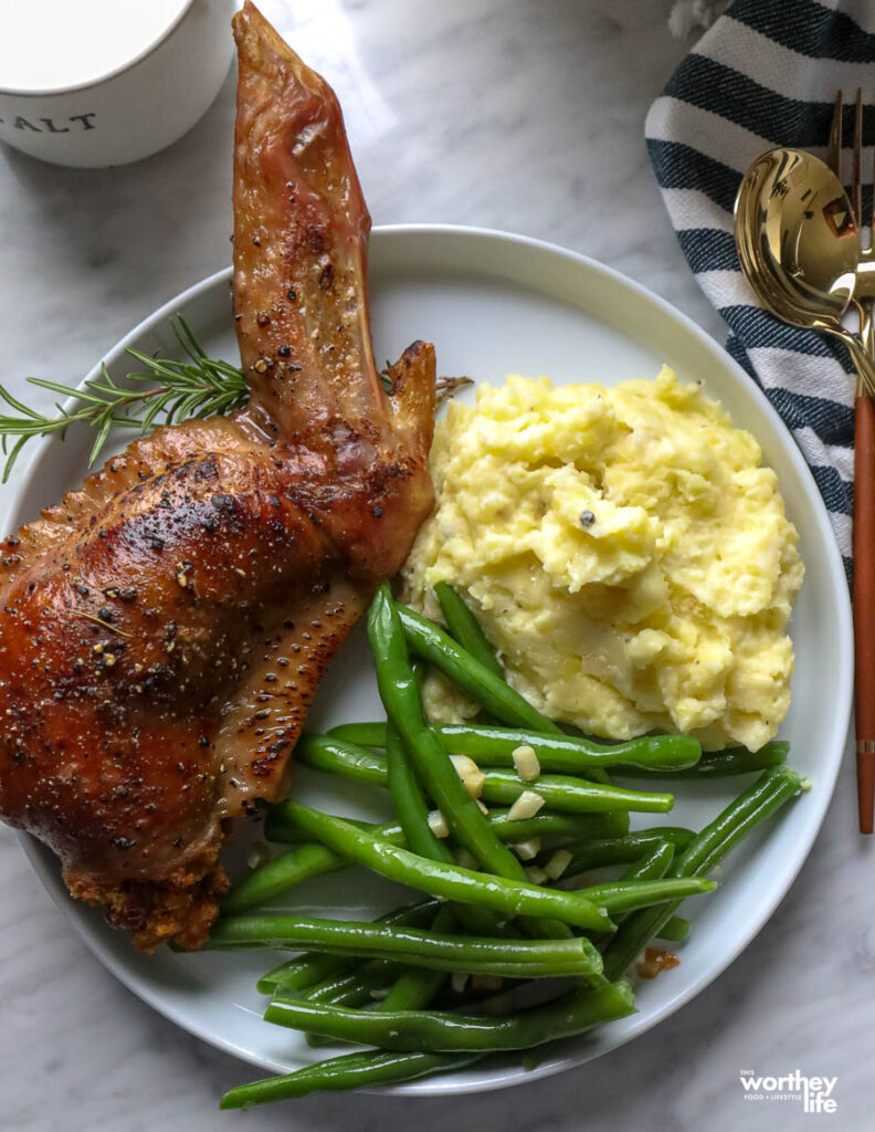 a white plate with a stuffed turkey wing, green beans, and potatoes