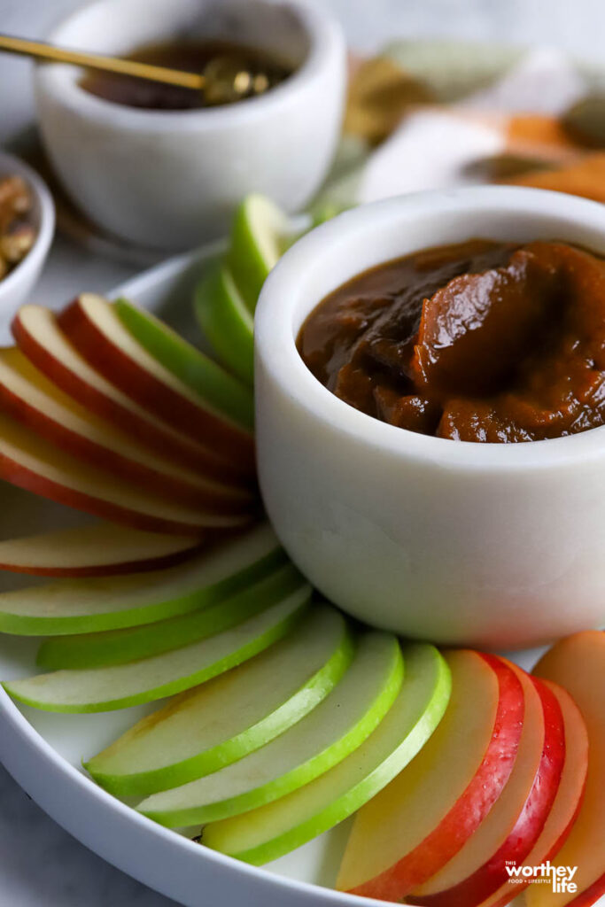 a cropped view of a white serving plate filled with apples slices and a serving bowl of pumpkin butter