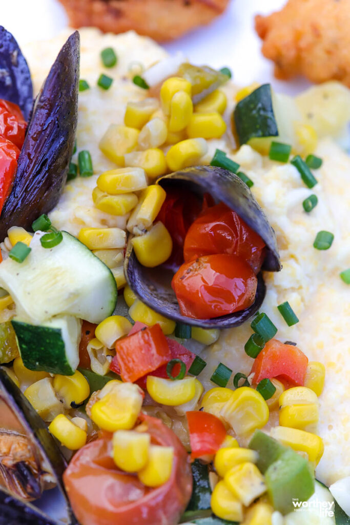 A plate of cheesy southern grits with vegetables and steamed mussels. 