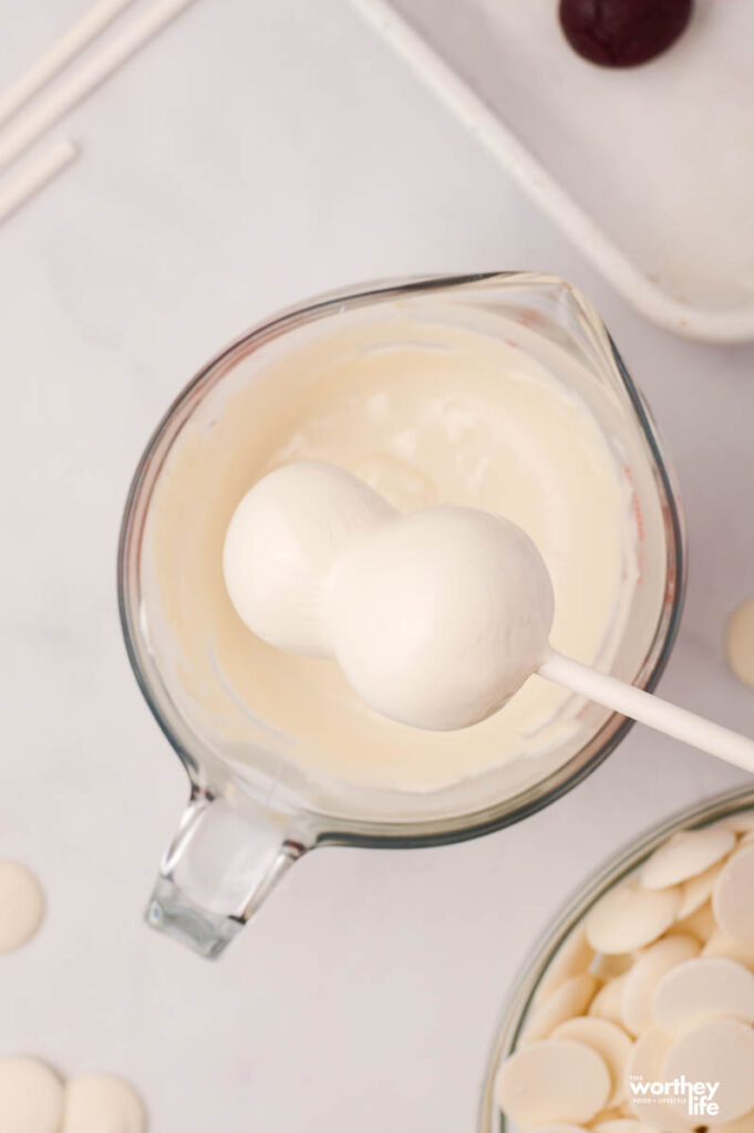 dipping edible snowman cake pops into white frosting