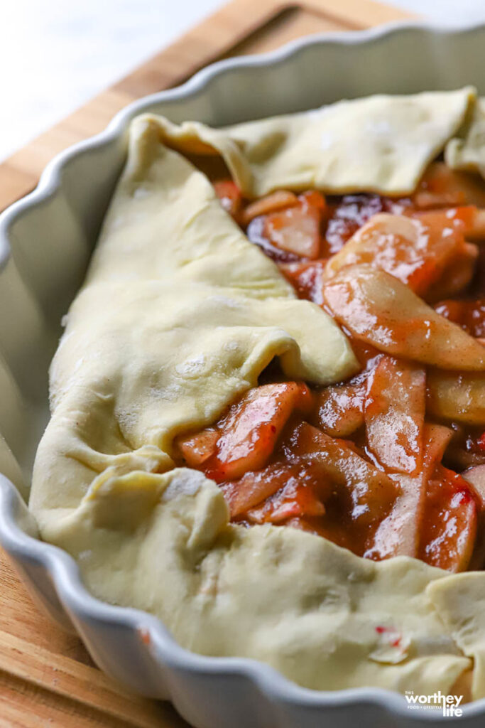 an unbaked apple and cranberry galette resting inside of a white pie pan