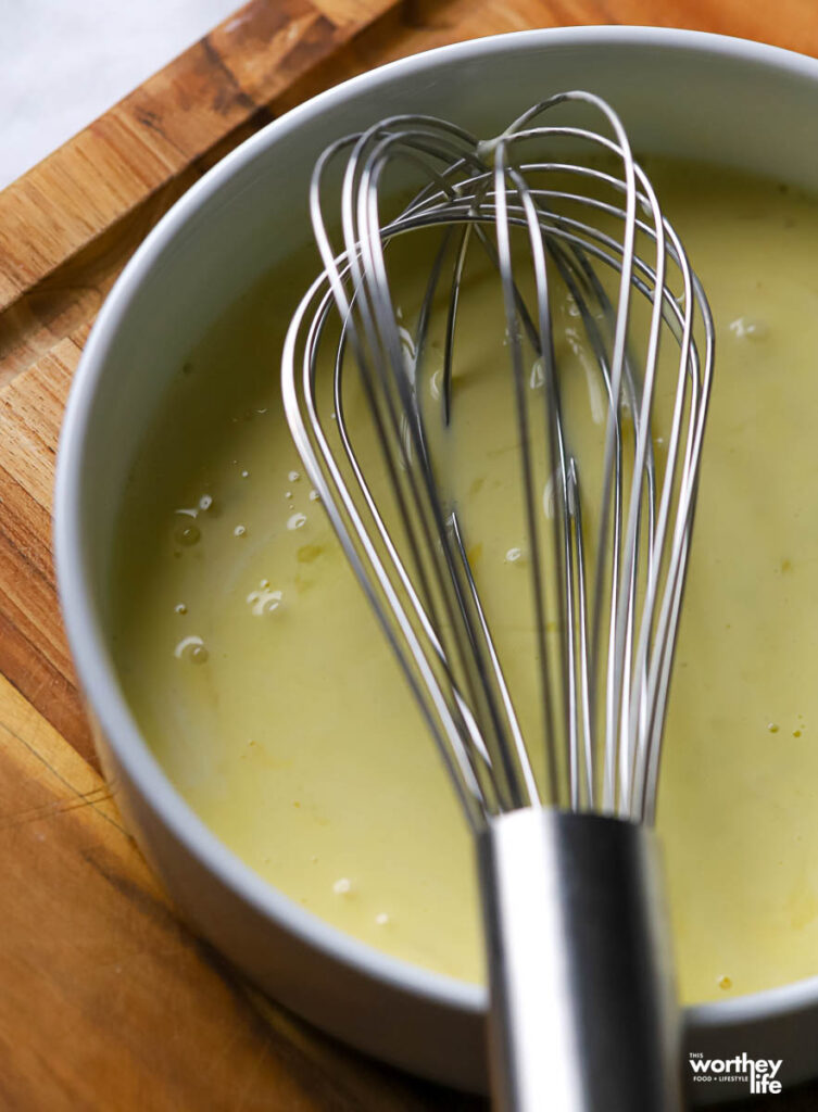 a white ramekin with egg wash and a wire whisk