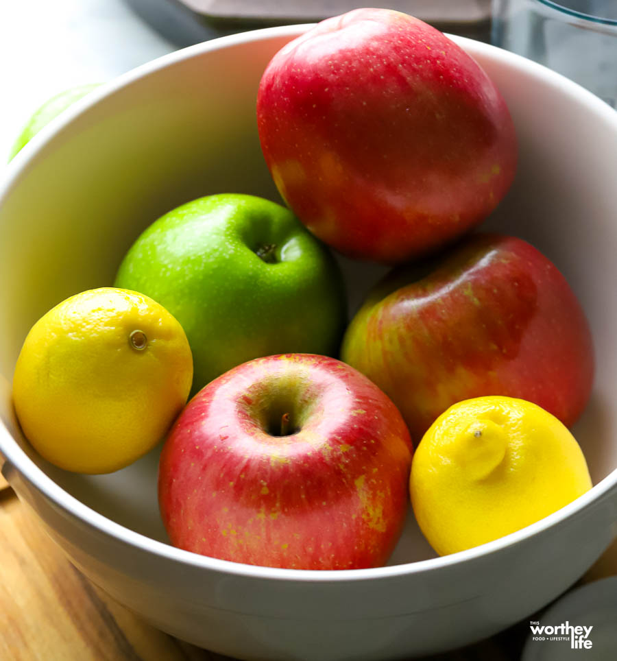 a white porcelain bowl with apples and lemons