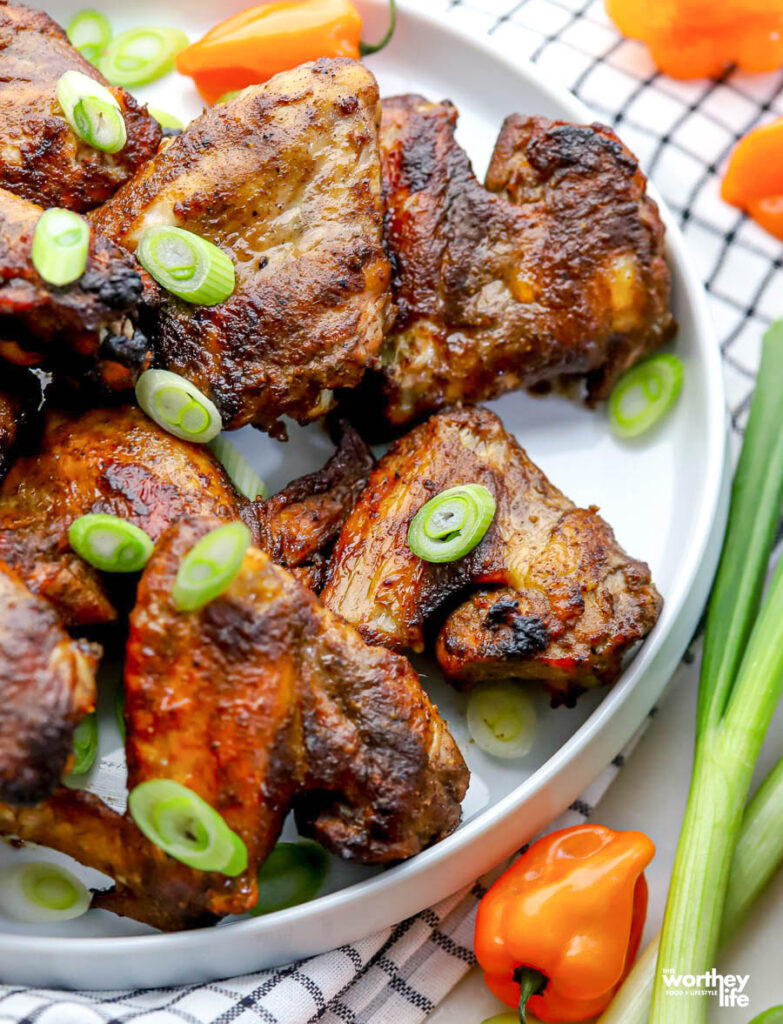 a white plate with several jerk chicken wings, peppers and scallions. 